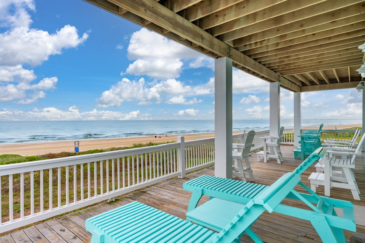 A wooden deck with a white railing overlooking a beach.