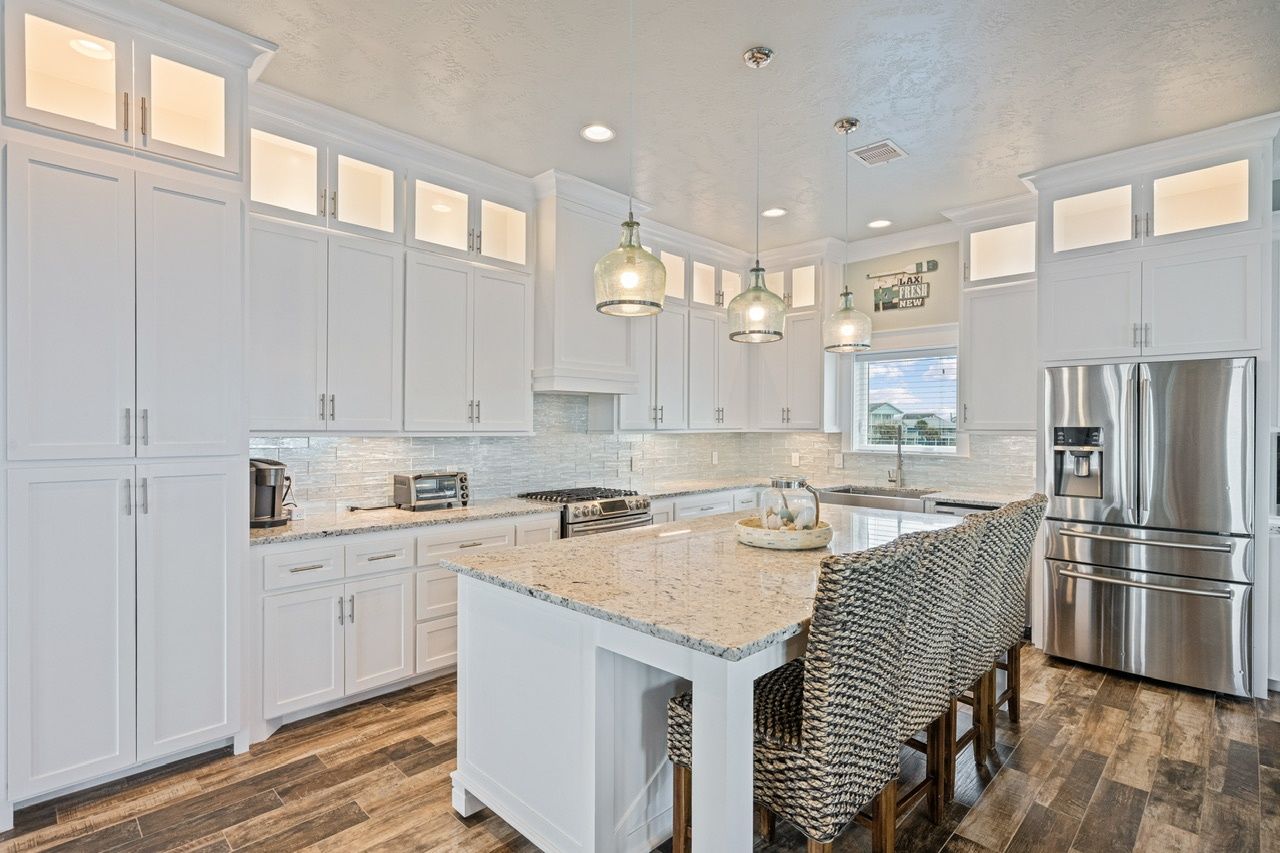 A modern kitchen with white cabinetry, a central island, stainless steel appliances, and pendant lighting.