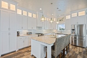 Une cuisine moderne avec des meubles blancs, un îlot central, des appareils en acier inoxydable et des luminaires suspendus.