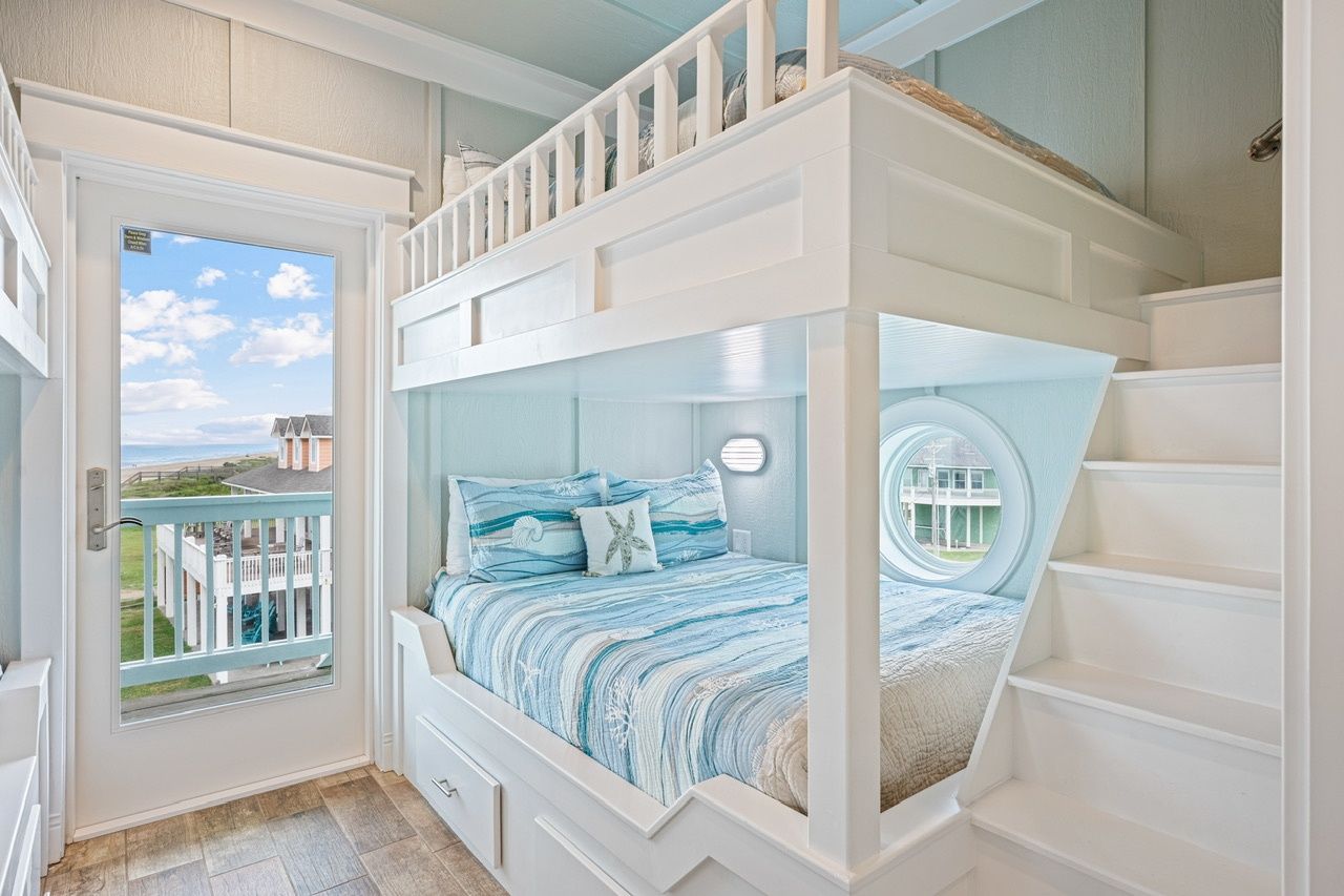 A bunk bed with a view of a house and beach through a door.