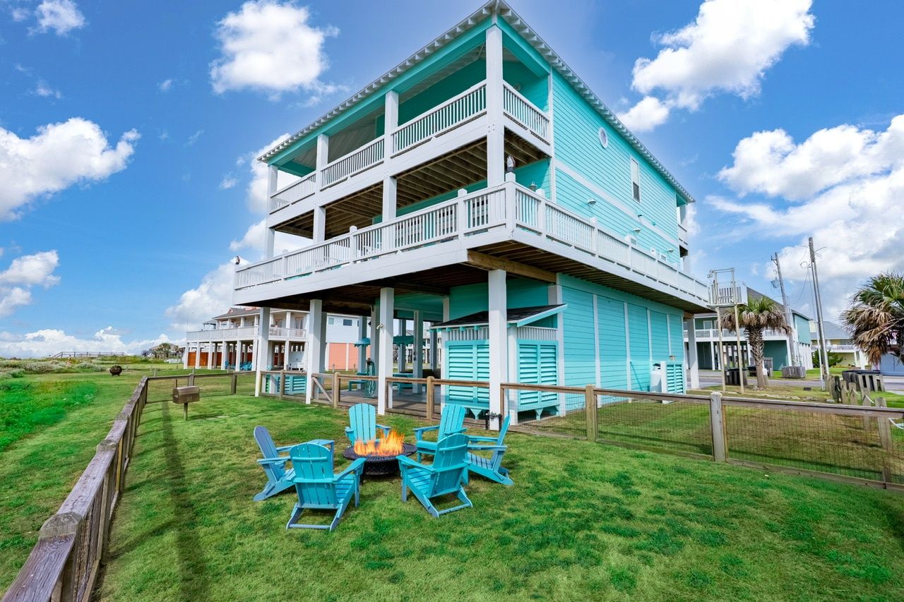A two-story building with a balcony, a fire pit with chairs, and a grassy area.
