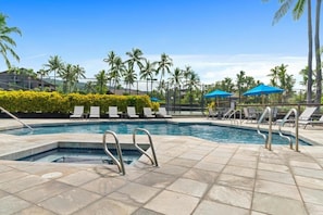 A swimming pool with lounge chairs and umbrellas, surrounded by palm trees and a clear sky. - Big Island Kanaloa At Kona 803 1 Bedroom Condo (Kailua-Kona)
