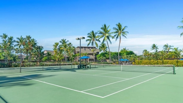 A tennis court with a net, surrounded by palm trees and a building in the background. - Big Island Kanaloa At Kona 803 1 Bedroom Condo (Kailua-Kona)