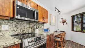 A kitchen with wooden cabinets, a stainless steel microwave, a built-in oven, and a granite countertop. - Big Island Kanaloa At Kona 803 1 Bedroom Condo (Kailua-Kona)