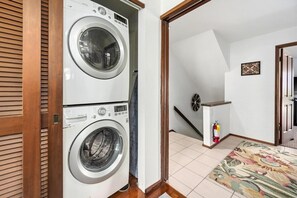 A laundry room with two front-loading washing machines, a fire extinguisher, and a patterned rug on the floor. - Big Island Kanaloa At Kona 803 1 Bedroom Condo (Kailua-Kona)