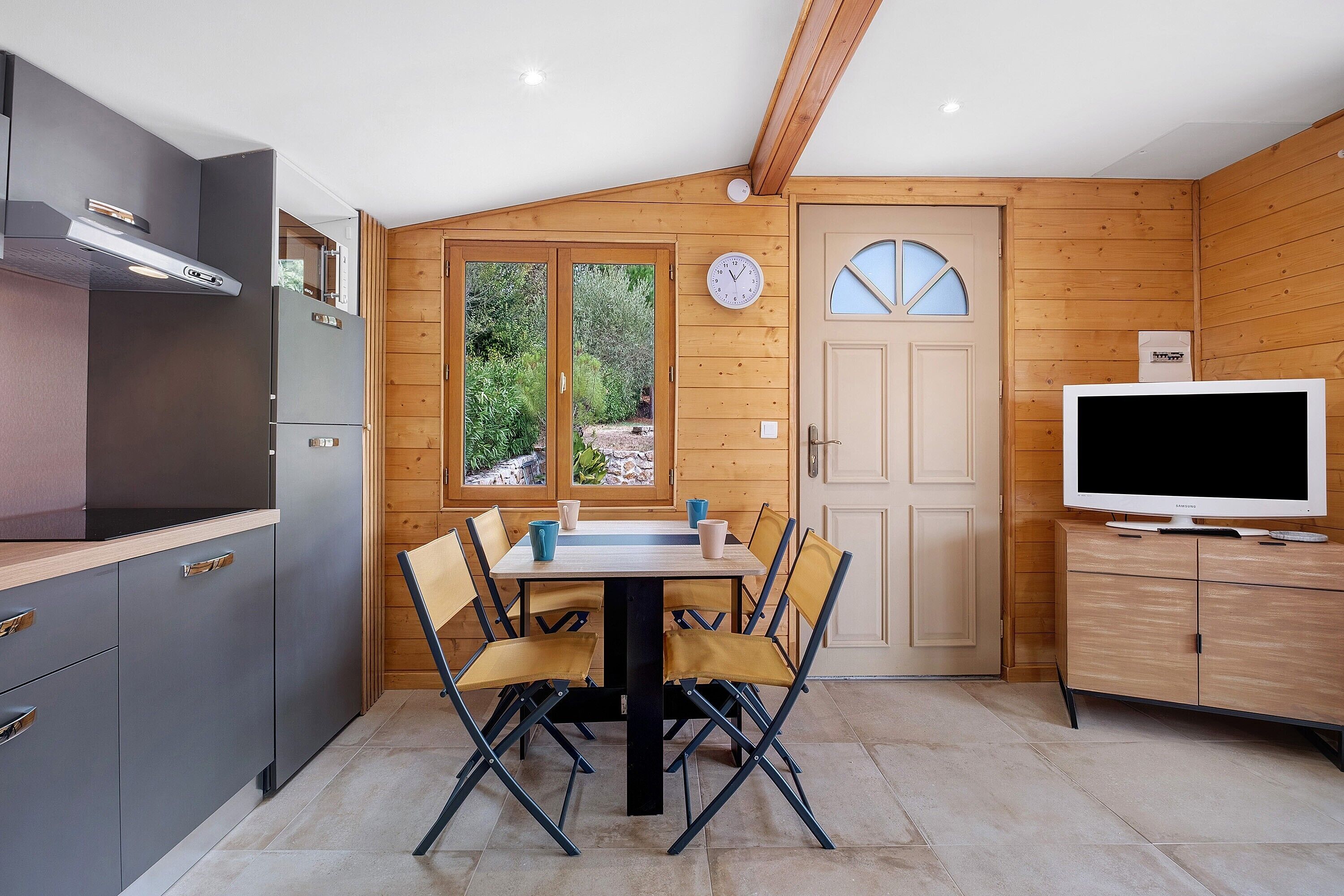 A compact kitchen with a dining table, chairs, a television, and wooden paneling.