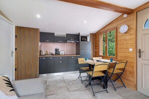 A compact kitchen with a dining area, wooden walls, and a window with greenery outside.