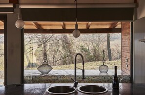 A kitchen with a built-in sink, a hanging light fixture, and a view of a wooded area through a window. - 'La Bolla Cottage' Vacation Home with Shared Pool, Wi-Fi, and Air Conditioning (Prignano sulla Secchia)