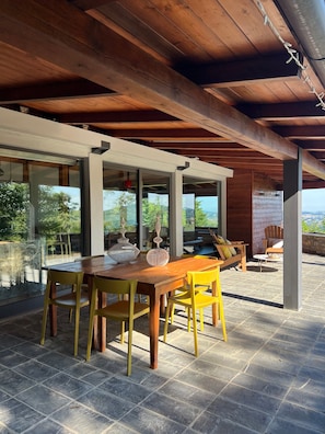 An outdoor dining area with a wooden table and yellow chairs, large windows, and a view of the landscape. - 'La Bolla Cottage' Vacation Home with Shared Pool, Wi-Fi, and Air Conditioning (Prignano sulla Secchia)