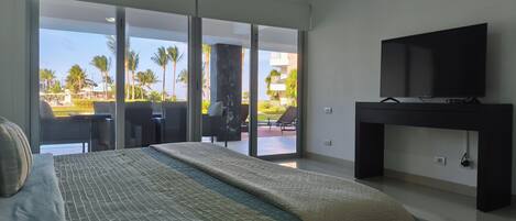 A hotel room with a bed, a TV on a stand, and a balcony with outdoor seating.