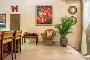 A dining area with a wooden table, wicker chairs, a potted plant, and a painting on the wall. - 3-bedroom Villa in beautiful Tabanan with rice field and river view (tabanan)