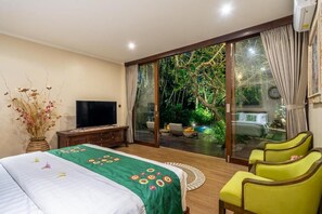 A bedroom with a bed, a television, a desk, and a view of a garden through a sliding door. - 3-bedroom Villa in beautiful Tabanan with rice field and river view (tabanan)