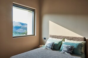 Ein Schlafzimmer mit einem Bett, Kissen, einem Nachttisch und einem Fenster mit Landschaftsblick.