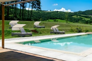 Ein Poolbereich mit Liegestühlen und Blick auf eine grüne Landschaft.