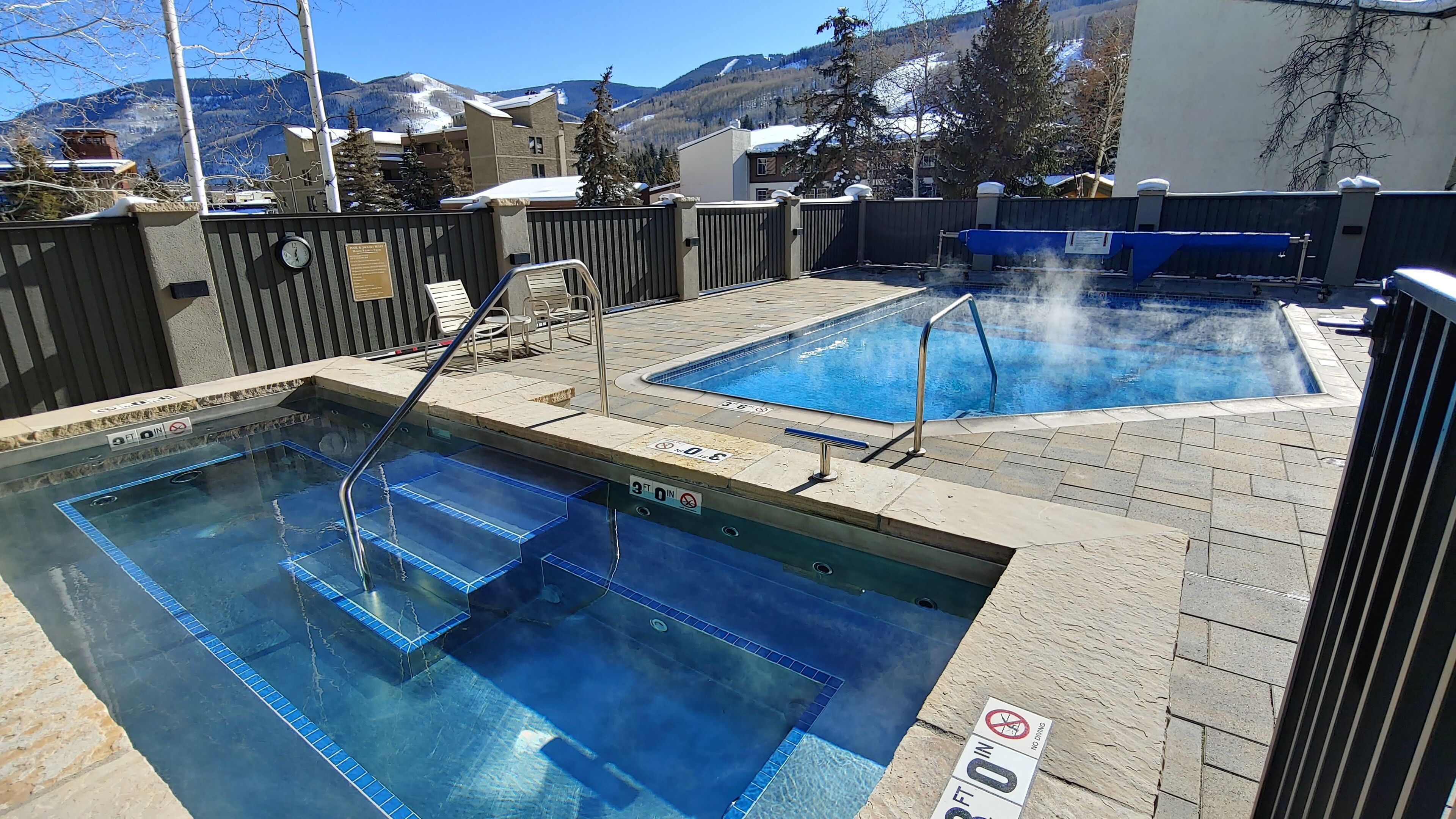 A pool area with two separate pools, a wooden fence, and a mountainous backdrop.