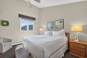 A bedroom with a large bed, a window with a view, a chair, a nightstand with a lamp, and two framed pictures on the wall. - Top-floor Ski Condo in Vail, walk to Gondola, W402 (Vail)