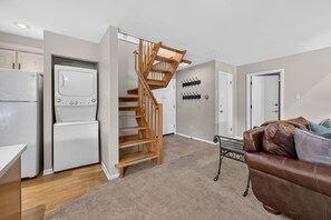 Eine moderne Küche mit eingebautem Kühlschrank und Herd, einer Holztreppe, einem Kleiderständer und einem Ledersofa in einem Wohnbereich.