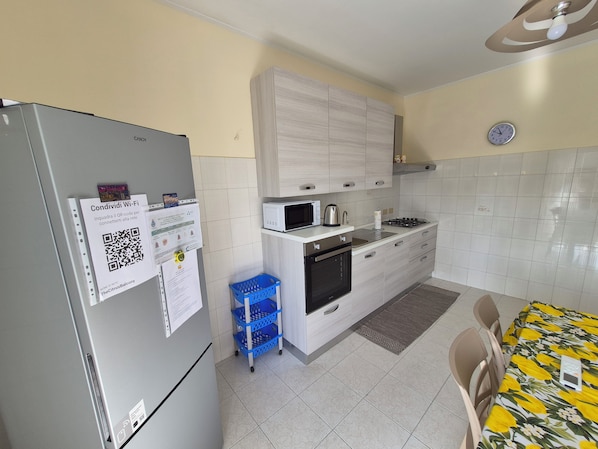 Una cocina equipada con refrigerador, microondas, estufa y pileta. Hay un código QR en el refrigerador y una cesta azul.