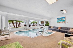 A pool area with a seating area, a painting of a beach scene, and a view of palm trees and a body of water. - Island Bay House A in Anna Maria Island (Holmes Beach)