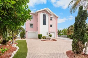 A two-story house with a pink exterior, a driveway, and a well-maintained lawn. - Island Bay House A in Anna Maria Island (Holmes Beach)