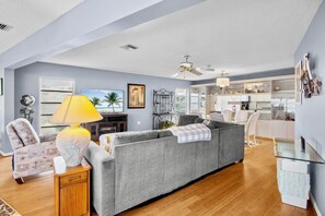 A modern living room with a grey sofa, a wooden side table, a lamp, and a television. - Island Bay House A in Anna Maria Island (Holmes Beach)