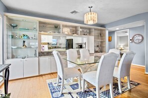 A modern kitchen with white cabinets, a glass dining table, and white chairs. - Island Bay House A in Anna Maria Island (Holmes Beach)