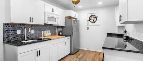 Una cocina moderna con armarios blancos, encimera negra, suelo de madera y un ventilador de techo.