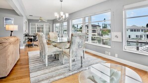 A spacious living room with a large window, a ceiling fan, and a dining area with chairs and a table. - Island Bay House B in Anna Maria Island (Holmes Beach)