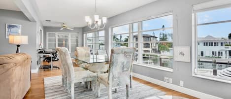 A spacious living room with a large window, a ceiling fan, and a dining area with chairs and a table.