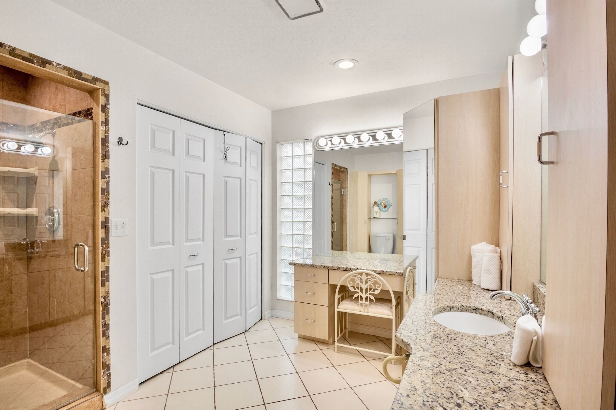 A bathroom with a shower, a vanity with a sink, and a mirror with lights.