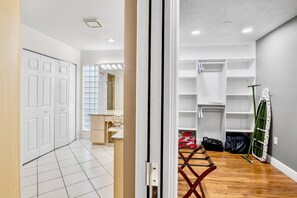 Ein modernes Interieur mit Fliesenboden, einem weißen Kleiderschrank, einem Schreibtisch mit Stuhl und einem Regal mit Taschen und einer Leiter.