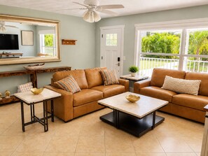 A living room with a brown leather sofa, a coffee table, and a television on a wall. - Private heated pool & hot tub near AMI and IMG (Bradenton)