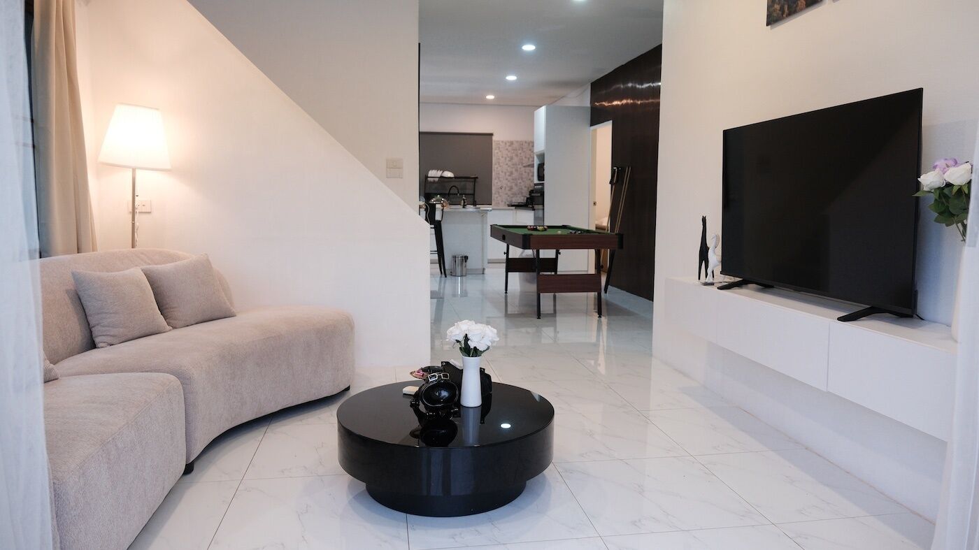 A modern living room with a sofa, a coffee table, a flat-screen TV, and a billiards table in the background.