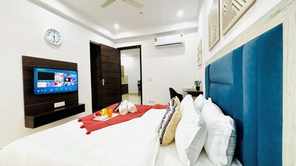 A hotel room with a flat-screen TV, a bed with white bedding, a red throw blanket, and a blue headboard.