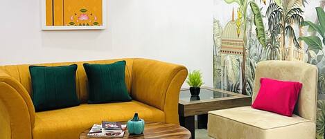 Una sala de estar con un sofá amarillo, un sillón color beige, una mesa de centro redonda y un ventilador de techo.