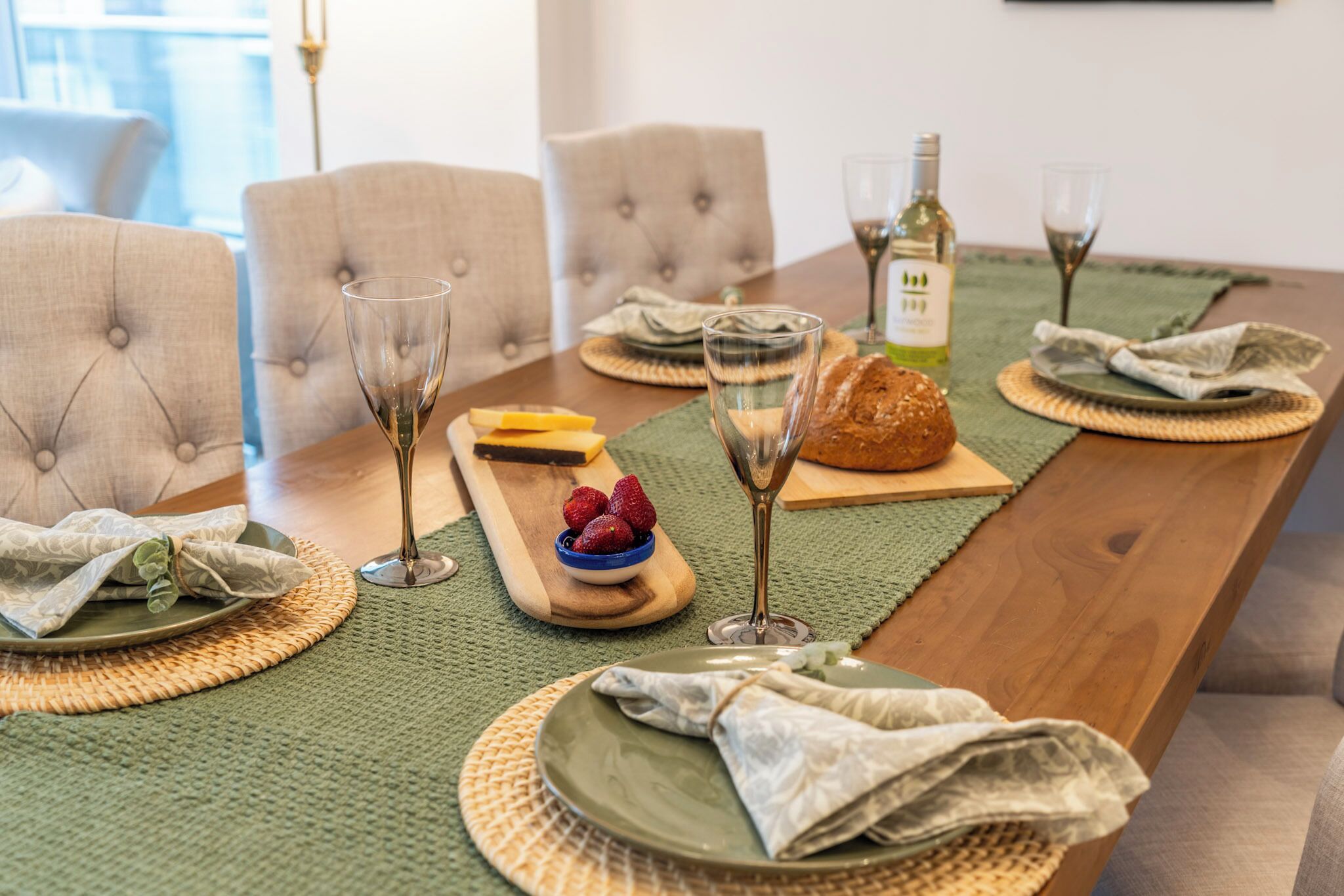 A dining table set with plates, glasses, a bottle, and a loaf of bread.