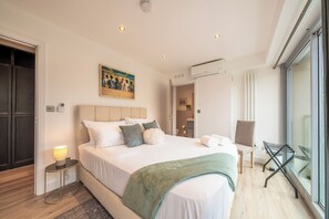 A modern hotel room with a large bed, a side table with a lamp, a chair, and a view of the outdoors. - Modern & Sleek 3BR, 2.5BA, Lift, AC, Centeral London (London)
