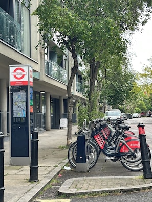 A map sign with cycle routes, a bike parking area, and a modern building with balconies. - Modern & Sleek 3BR, 2.5BA, Lift, AC, Centeral London (London)