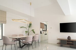 A modern dining area with a table and chairs, a hanging light fixture, a potted plant, and a television on the wall. - Vitsila Villa II, Design, Sea Views & Family Fun (Rethymno)