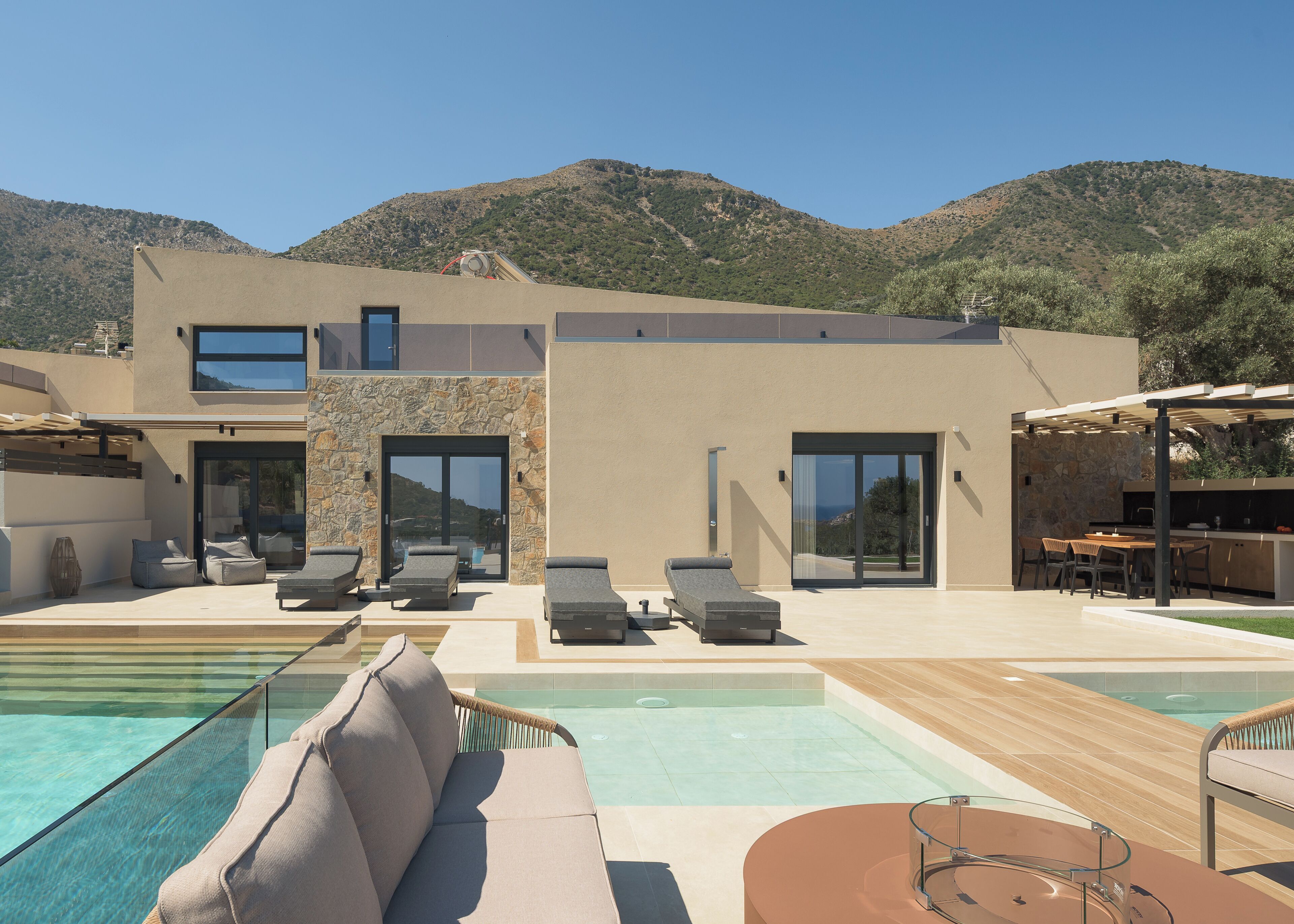 Una casa moderna con piscina, mobiliario de exterior y montañas al fondo.