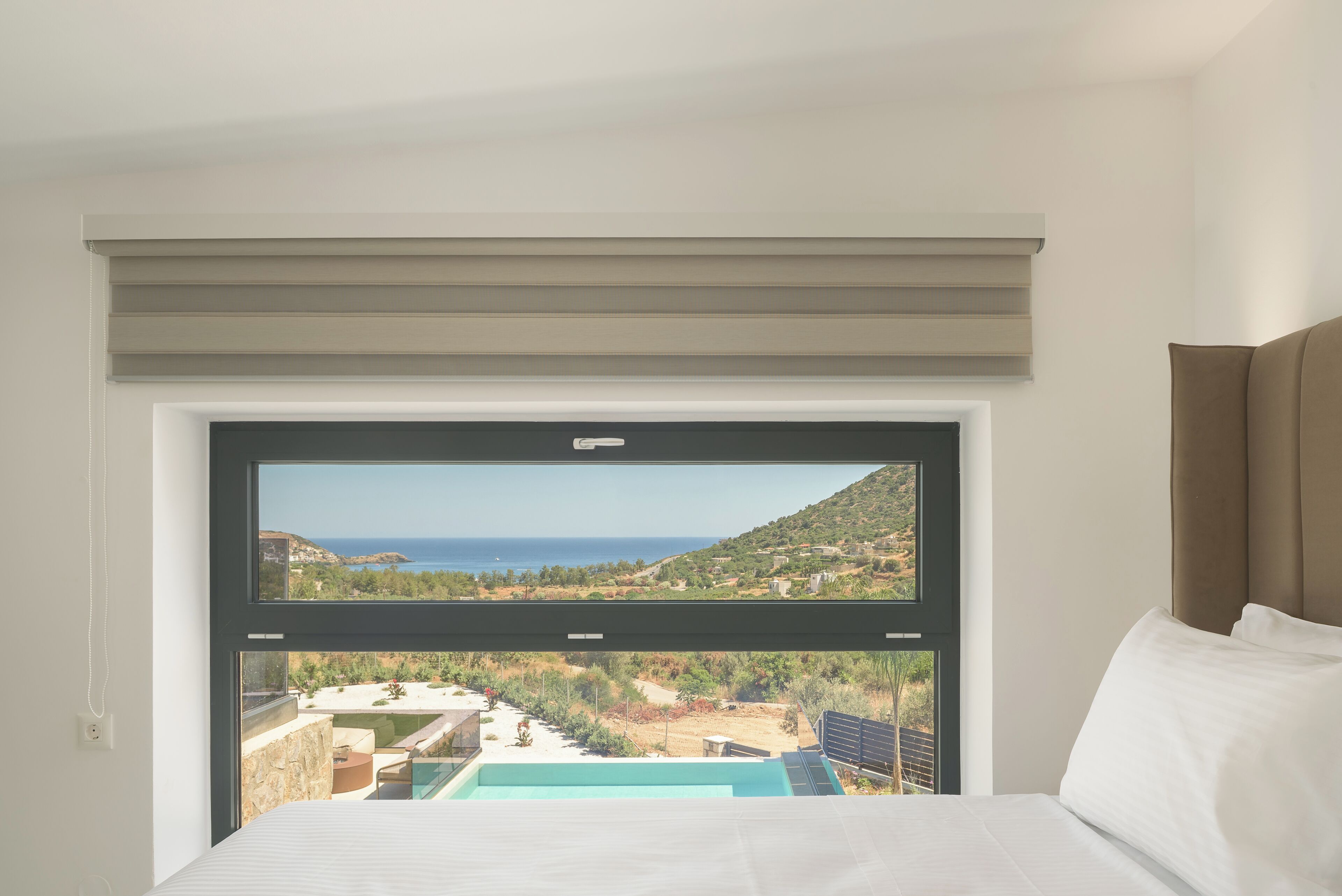 Ein Schlafzimmer mit einem großen Fenster, das Blick auf eine Küstenlandschaft und einen Swimmingpool bietet.