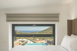 A bedroom with a large window offering a view of a coastal landscape and a swimming pool. - Vitsila Villa II, Design, Sea Views & Family Fun (Rethymno)