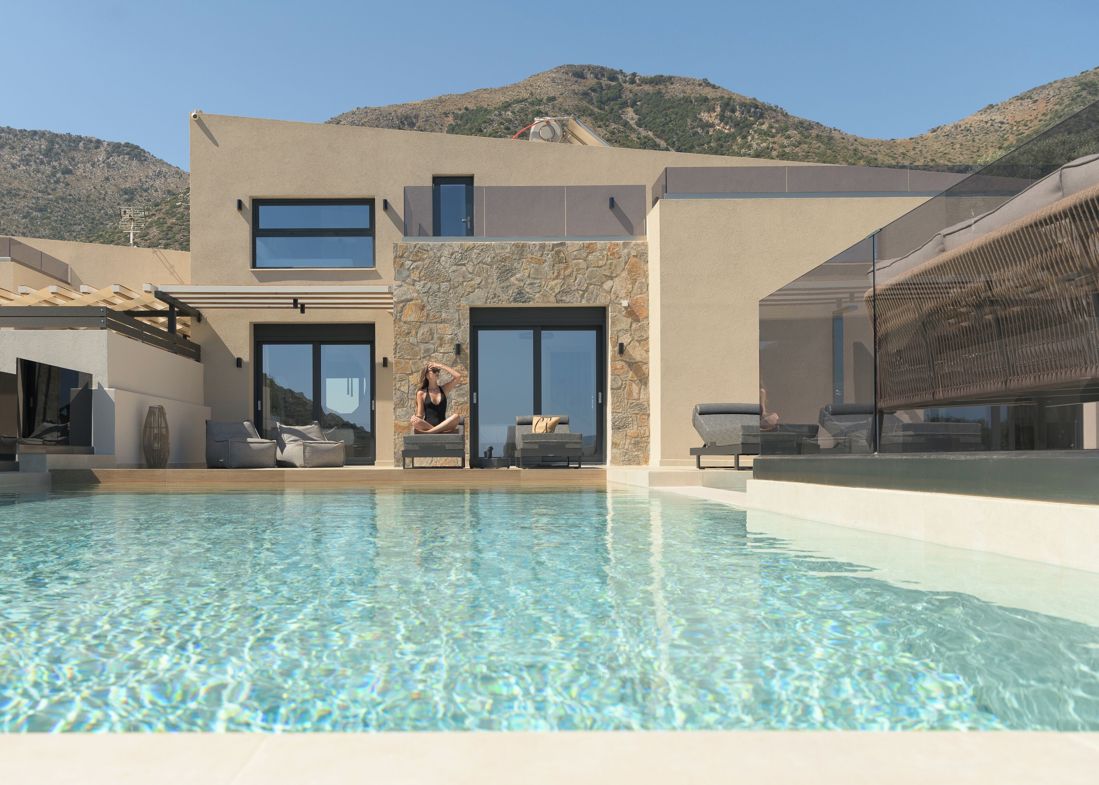 A modern building with a swimming pool, stone walls, and a view of a mountainous landscape.