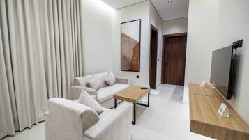 Quarto de hotel moderno com sofá, mesa de cabeceira de madeira, TV de tela plana e uma grande janela com cortinas.