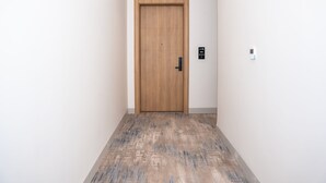 A hallway with a wooden door, a wall-mounted intercom, and a patterned floor.