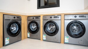 A row of General Coldin washing machines in a showroom with a tiled floor and a wooden cabinet.