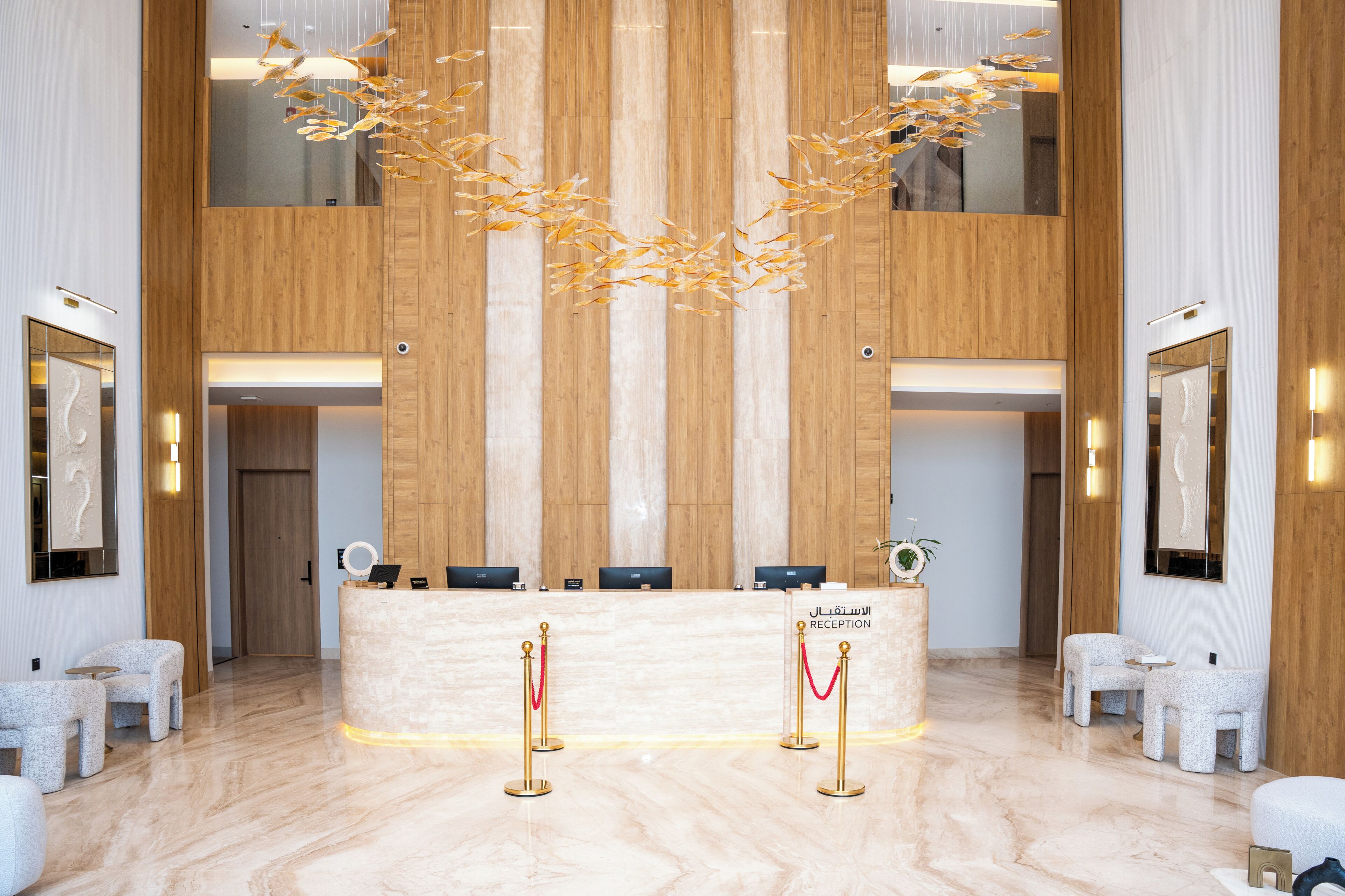 A reception area with a marble floor, wooden paneling, a reception desk, and two red stanchions with gold poles.