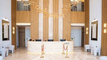 A reception area with a marble floor, wooden paneling, a reception desk, and two red stanchions with gold poles.