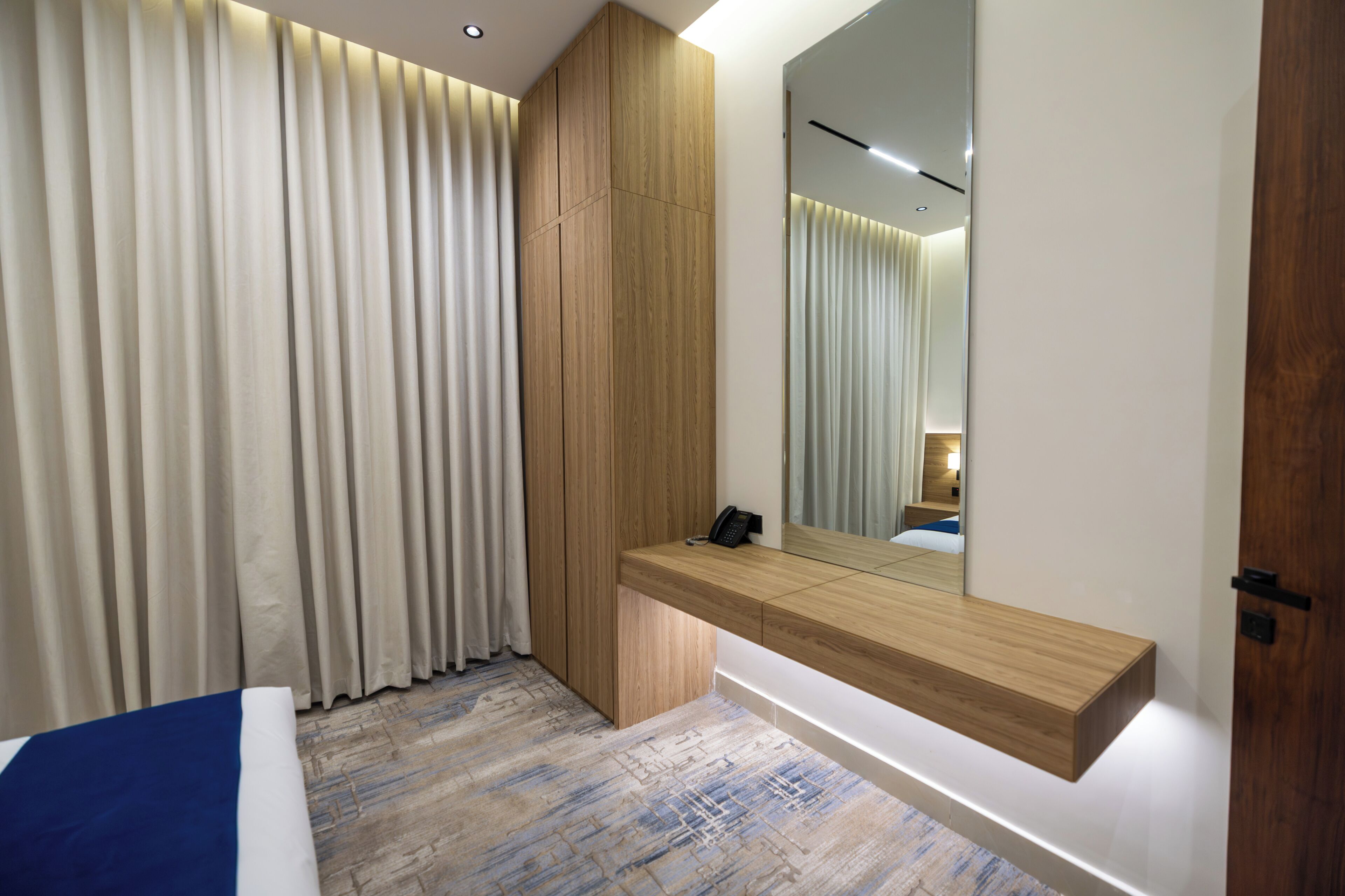 Un dormitorio moderno con una mesita de noche de madera integrada, un espejo grande y una cama con detalles azules.