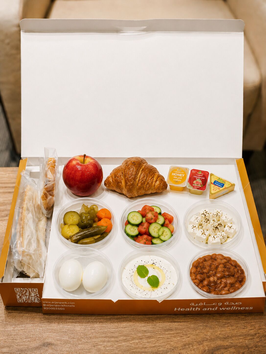 En matlåda som innehåller en croissant, ett äpple, ost, yoghurt och olika sorters sallad.